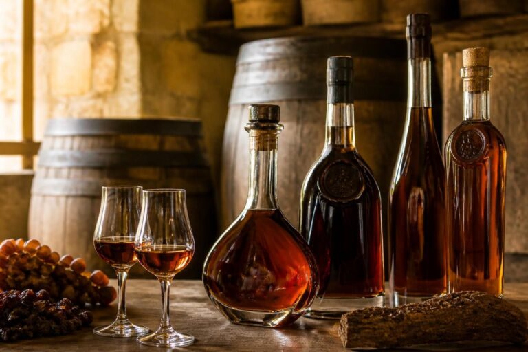 Dégustation de vieil armagnac : verres tulipe avec eau-de-vie ambrée, bouteilles et fûts de vieillissement en cave