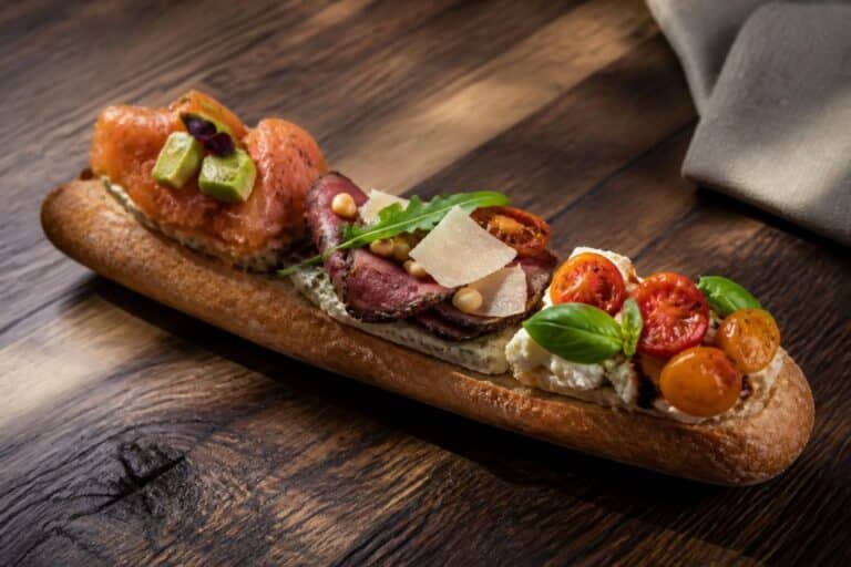 Baguette garnie de saumon, viande, tomates, fromage et basilic sur une table en bois