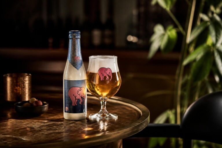 Bouteille de bière avec éléphant rose et verre ambré sur une table